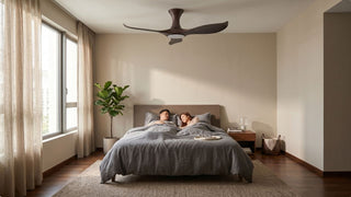 Hugger ceiling fan in a warm Singapore bedroom with low ceiling, wood bed frame, grey bedding, and soft natural light
