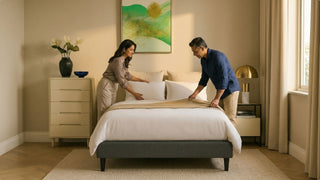 Couple making a bed with an Iuiga-style frame in a cosy Singapore bedroom with warm natural light
