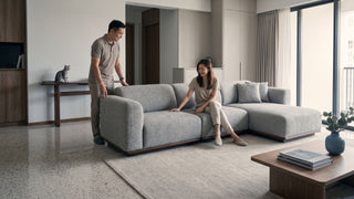 Couple checking a large grey sectional sofa inside a spacious jumbo flat living room before furniture delivery completion