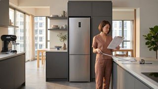 Woman measuring a kitchen countertop beside a stainless steel fridge in a modern Singapore kitchen with open dining area