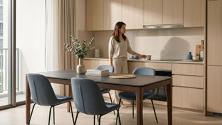 Woman standing in a modern Singapore open-plan kitchen with a built-in kitchen hood above the hob and dining table nearby.