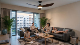 Family relaxing in a Singapore living room with large ceiling fan, grey sofa, and balcony view