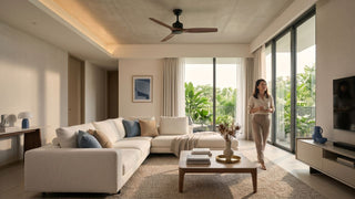 Large ceiling fan above a bright modern condo living room with beige sofa, balcony greenery and warm natural light.