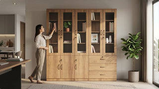 Woman styling books in a large wooden bookcase with glass doors in a warm modern Singapore home