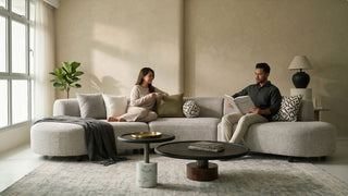 Couple relaxing on a light grey curved sofa with round coffee tables, soft cushions and warm neutral living room decor