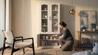 Woman organising jars in a light wood display cabinet with glass doors in a cosy Singapore living room with chair and wall art