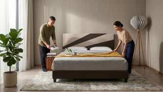 Couple arranging a low king bed frame with patterned rug, floor lamp, and neutral bedroom decor