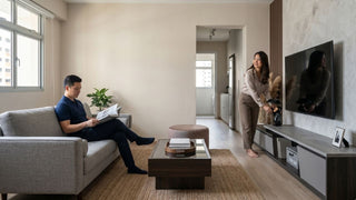 Couple styling a low TV console in a cosy Singapore living room with grey sofa and coffee table