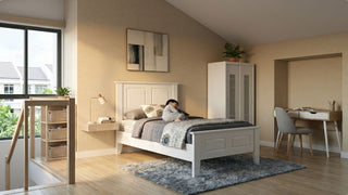 Child resting in a maisonette children’s room with white bed frame, study desk, wardrobe, shelves, and warm natural light
