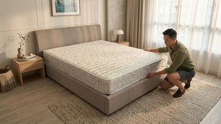 Man checking mattress support on a grey bed frame in a cosy Singapore bedroom