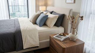 Neutral Singapore bedroom with upholstered bed, layered pillows, wooden bedside table, and soft daylight for a mattress shop guide