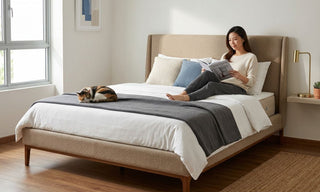 Woman reading on a beige bed with a cat in a bright Singapore bedroom, showing comfortable mattress height for a small home.