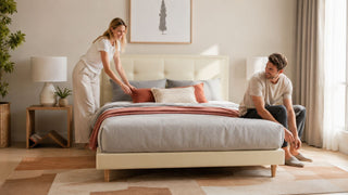 Cream upholstered bed frame in a modern Singapore bedroom with a couple arranging pillows for a practical, comfortable home setup.