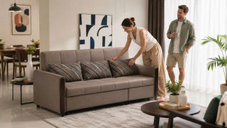 White couple arranging cushions on a taupe sofa in a bright modern Singapore apartment living room.