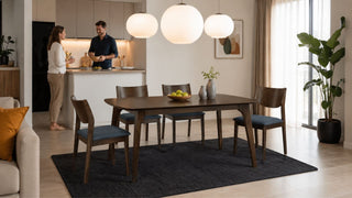 MegaFurniture dark wood dining set in a bright Singapore condo dining area with a relaxed couple preparing the space.