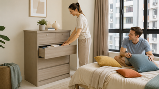 White couple organizing folded clothes in a light wood chest of drawers in a modern Singapore condo bedroom.