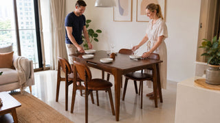 Extendable wood dining table set in a bright Singapore condo dining area with a couple preparing the table for guests.