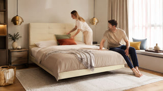 Cream upholstered floating bed frame in a modern Singapore bedroom with a couple arranging cushions.