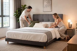 Charcoal grey upholstered floor bed frame in a modern Singapore condo bedroom with a couple arranging bedding.