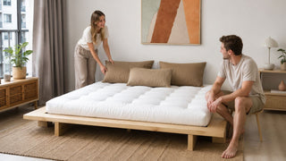 Modern futon bed in a bright Singapore apartment bedroom with a couple arranging cushions for everyday comfort