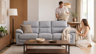 Light grey three-seater sofa in a warm Japandi living room with a couple arranging cushions in a Singapore home.
