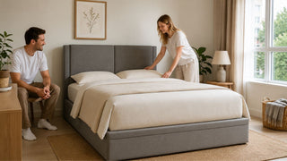 Grey upholstered bed in a bright Singapore bedroom with a couple arranging bedding for better mattress comfort.