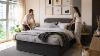 White couple arranging bedding on a modern grey upholstered bed frame in a bright Singapore condo bedroom