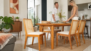 Rattan dining chairs around a wooden table as a couple prepares a modern Singapore home dining area