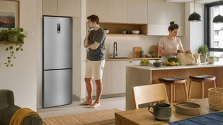 Silver bottom-freezer refrigerator in a modern Singapore kitchen with a couple considering a repair or replacement decision.