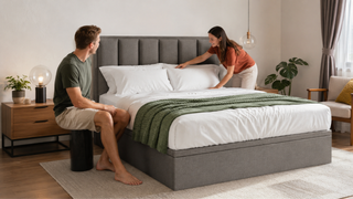 Grey upholstered bed frame in a modern Singapore bedroom as a couple arranges pillows and bedding for a practical home setup.