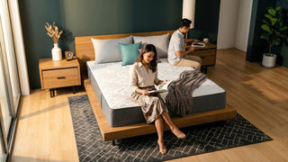 Couple relaxing on a memory foam mattress in a warm Singapore bedroom with wood bed frame, dark accent wall, and bedside tables