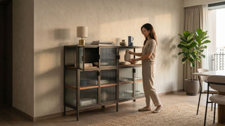 Woman arranging decor on a metal cabinet with fluted glass doors in a warm Singapore condo living and dining area.