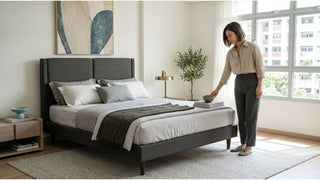 Woman styling a minimalist bedroom with grey upholstered bed frame, neutral bedding and HDB window view