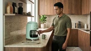 Man using a mint green coffee machine in a compact HDB kitchen with wood cabinets and coffee accessories