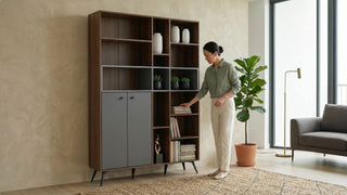 Modern wooden display shelf with grey cabinet doors, books, vases and plants styled beside a sofa in a warm living room
