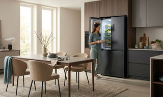 Woman using a large black refrigerator in a modern Singapore kitchen with dining table and warm neutral interiors
