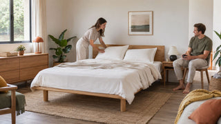 Modern wooden Muji-style bed frame in a bright Singapore bedroom with a couple arranging neutral bedding