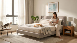Natural latex mattress in a bright Singapore bedroom with neutral bedding, two cats, and a woman reading by the bed.