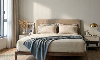 Neutral Singapore bedroom with beige bedsheets, upholstered headboard, blue throw blanket, and warm natural light.