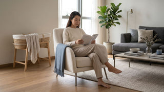 Expectant mother reading in a supportive cream feeding chair beside a baby bassinet in a Singapore living room.
