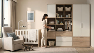 Mother organising baby clothes in a modular nursery wardrobe beside a cot and nursing chair in a warm Singapore home.