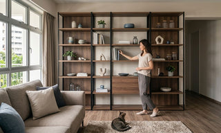 Woman styling a large open shelf cabinet with books, ceramics, plants, and closed storage in a Singapore HDB living room.