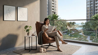 Woman reading on a brown outdoor lounge chair in a Singapore condo balcony with side table, plant and pool view.