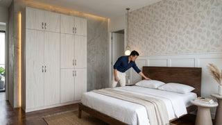 Man styling a bed beside a light wood wardrobe in a modern Singapore bedroom