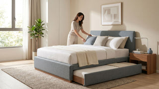 Woman arranging pillows on a grey fabric pull-out bed frame with trundle mattress in a bright Singapore bedroom.
