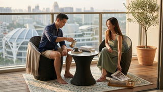 Couple enjoying coffee on black rattan balcony chairs with round table, outdoor rug, planter, and Singapore city skyline view