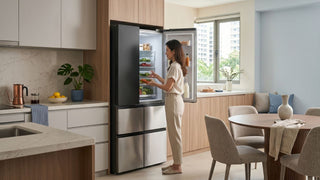 Woman organising food in an open refrigerator in a modern Singapore kitchen with dining area nearby.
