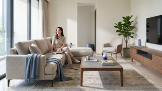 Woman sitting on beige sofa in a bright Singapore condo living room with coffee table, TV console, and neutral furniture.