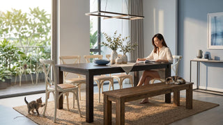 Woman reading at a dark wood dining table with bench seating and cats in a bright Singapore home.