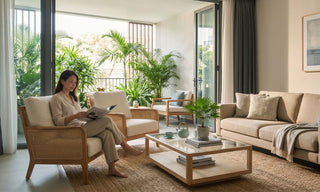 Woman reading in a resort-style Singapore living room with rattan armchair, beige sofa, indoor plants, sheer curtains and natural woven rug.